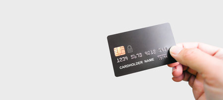 Hand holding luxury credit card on grey background, hand showing black credit card for online...