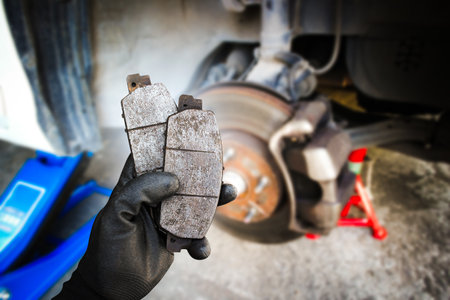 Used car brake pads in the hands of a mechanic with brake discs and brake calipers on the background , Car spare parts and maintenance conceptの写真素材