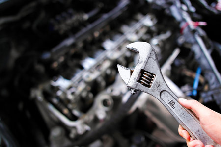 Adjustable wrench or adjustable spanner in a car mechanic hand with car engine blurred background , Car maintenance service conceptの写真素材