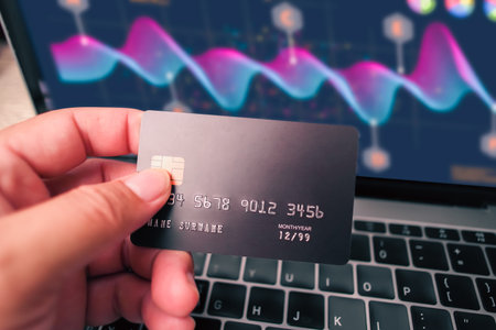 Close up of human hand holding credit or debit card and business graph in laptop blurred on...