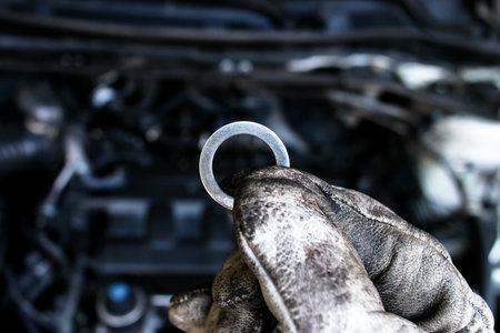 Metal flat washer for use in automotive repair , Mechanic holding metal washer above engine , Car...