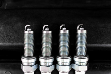 Car Spark Plugs, Close-up of four new iridium spark plugs are lined up against a dark background....