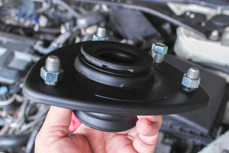 Top Strut Mount, A close-up of hand holds a black automotive strut mount with visible bolts over a...