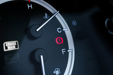 Red brake system warning light on car dashboard next to fuel and temperature gauge indicators.