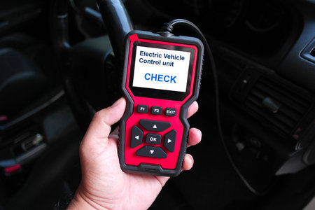Hand holding an OBD2 scanner device for electric vehicle diagnostics, displaying Electric Vehicle...