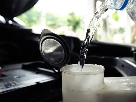 Pouring clean water into car windshield washer reservoir tank under the hood, vehicle maintenance and windshield washer water refill conceptの写真素材