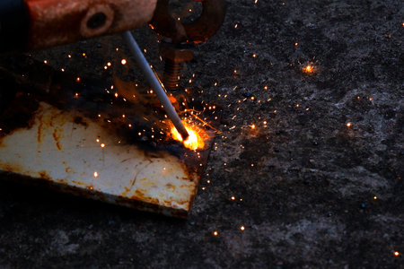 Close-up of metal welding process with bright sparks and molten steel, industrial fabrication and repair work concept, welder using electrode rod on rusty metal surfaceの写真素材