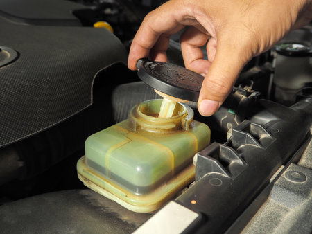 Mechanic hand opening power steering fluid reservoir cap in a car engine bay, checking fluid level during vehicle maintenance, automotive service and hydraulic steering care conceptの写真素材