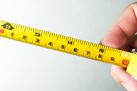 Precision Tape Measurement Tools, A hand holds a yellow retractable tape measure, showing markings...