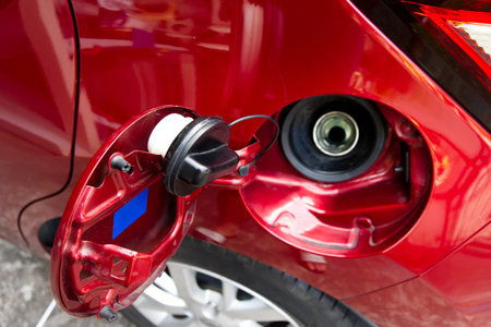 Car Fuel Tank Inlet, The fuel door of a red car is open, revealing the black gas cap and the metal filler neck ready for refueling at a gas station.の写真素材