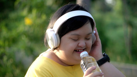 While exercising in the park, an Asian girl with down syndrome uses a water bottle as a microphone.の写真素材