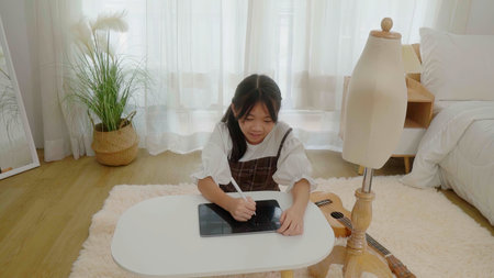 Asian young girl use tablet to find reference to design clothes in bedroom.の写真素材
