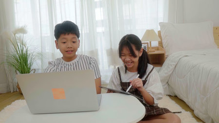 Boy using laptop looking at girl using pen write tablet in bedroom.の写真素材