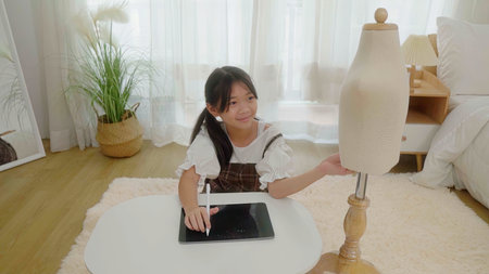 Asian young girl use tablet to find reference to design clothes in bedroom.の写真素材