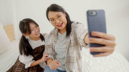 Asian female teachers use smartphones to take selfies with student kid girl in bedroom.の写真素材