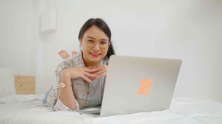 Happy asian beautiful freelance woman using laptop business online  in bed at home.の写真素材