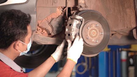 Asian man car mechanic replacing a car tire in garage workshop. . Auto service, Car-care center removes the wheel, Repair and maintenance of the car in service.の写真素材
