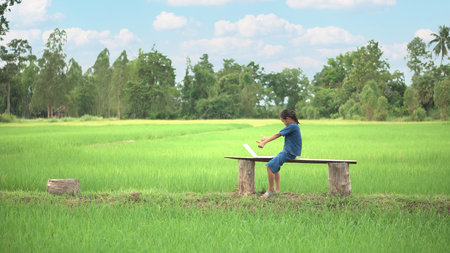 Asian girl live streaming on smartphone or laptop in rice field, countryside of Thailand.の写真素材