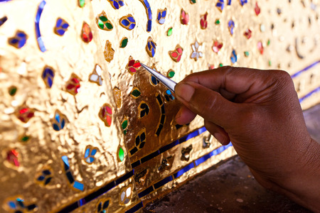 Hand of artist decorating the base of the image of Buddha with stained glass