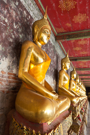 golden buddhas lined up along the wall in templeの写真素材