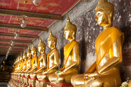 golden buddhas lined up along the wall in templeの写真素材