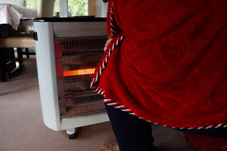 Man getting warm with an electric heater. Covered with a red blanket.