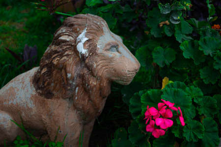 A lion statue on a garden in front of a pinkish flowerの写真素材