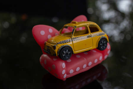 A yellow taxi cab sitting on a white dotted red toy couch. Symbolizing comfort of the taxies.の写真素材