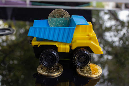 A yellow turquoise colored toy truck carrying and dropping off some bitcoins.の写真素材