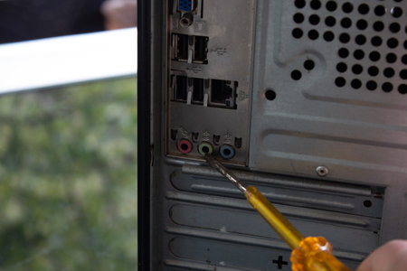 Pointing out the back sockets of a home computer with a yellow transparent screwdriver.