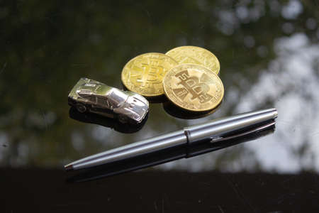A shiny silver car with some bitcoin and a silver pen on a shiny black surface.の写真素材