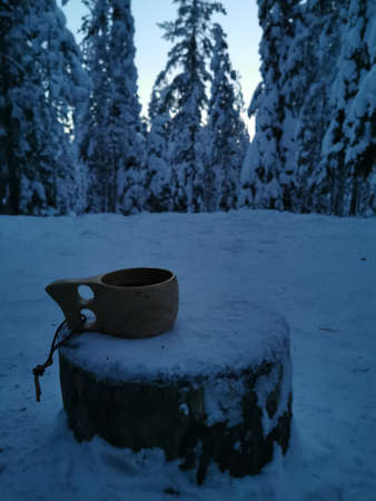 A kuksa wooden cup filled with hot tea on a fence with a snowy mountain view at morning sun.の写真素材