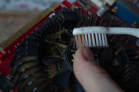 Man hand with a dirty toothbrush cleaning a rusty and old graphic card on a wooden cutting board....