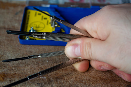 Man hand holding some small screwdrivers set in a blue plastic box on a wooden cutting board with some screws around them. Order of technology.の写真素材