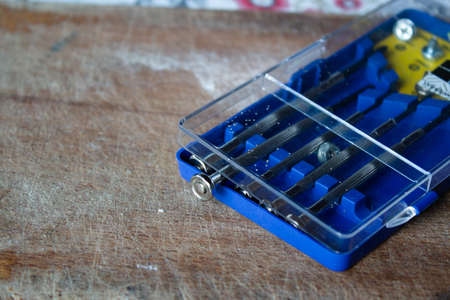 Man hand holding some small screwdrivers set in a blue plastic box on a wooden cutting board with...