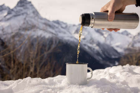 A hand filling a cup with some tea at a beautiful snowy mountain view. Break from daily life and recovery moments.の写真素材