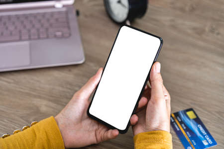 Women hands holding Mobile Phone with blank screen and Credit Card on office desk and using mobile...