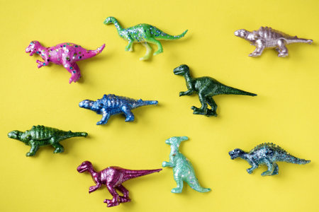 Colorful toy dinosaurs on yellow surfaceの写真素材