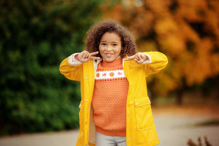 Portrait of cute adorable little girl child making funny silly faces, showing tongue, in autumn fall park outside, playing having fun, lifestyle childhoodの写真素材