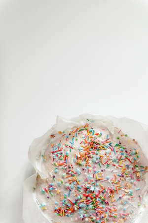 Easter cake, sweet bread decorated with white glaze and colored meringue. Kulich wrapped in a craft paper on the white background.の写真素材