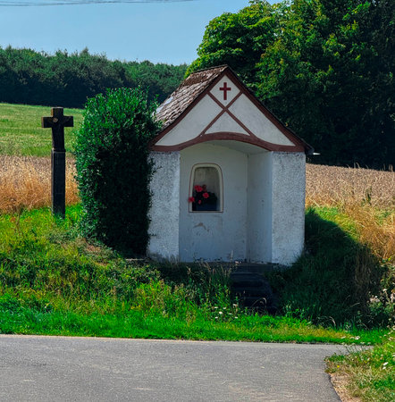 Old stone chapel with bell gable and tiled roof in green field under cloudy skyの写真素材