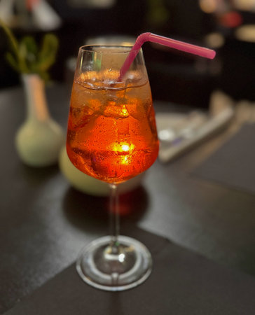Glowing orange cocktail with ice in a wine glass on a dark table. Warm evening light creates a cozy bar moodの写真素材