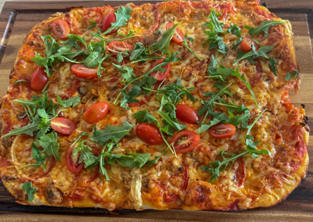 Homemade rectangular pizza topped with fresh arugula and cherry tomatoes. Golden baked crust with melted cheese creates an appetizing lookの写真素材