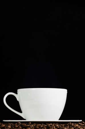 Cup of coffee stays on coffee beans over dark background. Side view.の写真素材