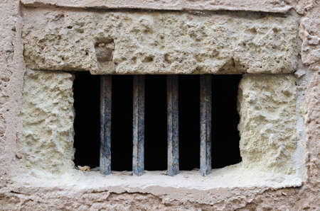 Window with iron bars on old facade with white bricks