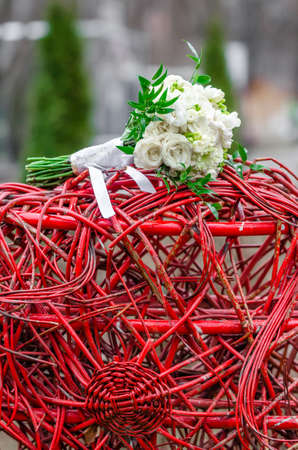 Brides bouquet of white rose on wedding day lays on red heartの写真素材