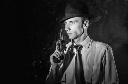Handsome detective in trench coat holding a gun in the dark. Noir film style. Black and white photographyの写真素材