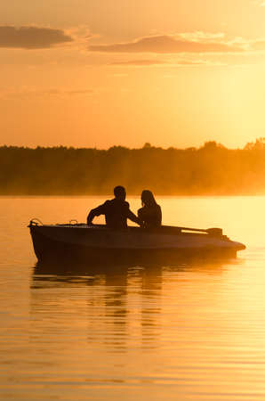 Romantic golden river sunset with fog and loving couple on small boat backlit by sunlightの写真素材