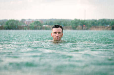 Middle aged man swimming in lake with blue water under the rain in thunderstormの写真素材