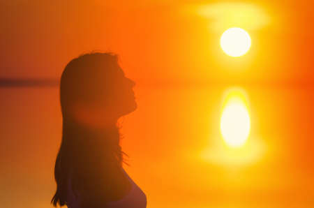 Beautiful female model enjoying sunsetat seaside. Calm water of salt lake Elton reflects silhouette of woman. Sun goes under horizon. Girl stands alone in water. Sun reflects in Elton's water.の写真素材